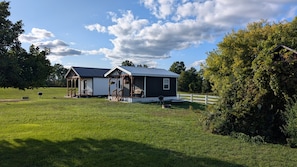 A two-story house with a porch, a fenced yard, and a large tree. - Cabin Alice, 1-bedroom cabin in the heart of Amish Country in charming Clare (Clare)