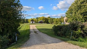 Ein Kiesweg führt zu einem Gebäude mit einer Veranda, umgeben von Grünflächen und Bäumen.
