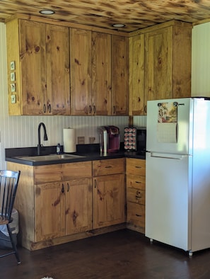 A kitchen with wooden cabinets, a stainless steel sink, a coffee maker, and a refrigerator.