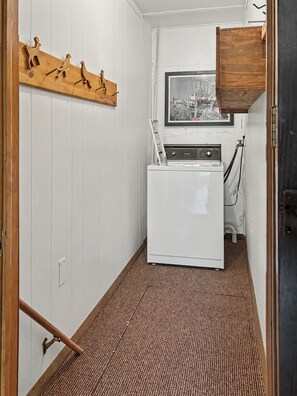 A compact laundry room with a white washing machine, a wooden drying rack, and a framed picture on the wall. - Cozy 2-bedroom cottage in serene Lakewood (Lakewood)