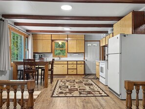 A kitchen with wooden cabinets, a dining table with chairs, a refrigerator, and a window with curtains. - Cozy 2-bedroom cottage in serene Lakewood (Lakewood)