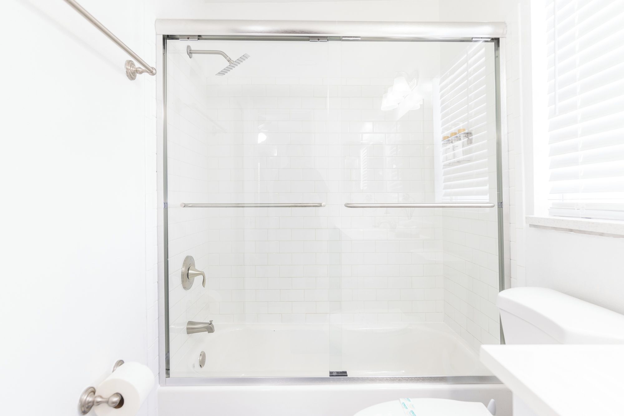 A glass-enclosed shower with a handheld showerhead, a towel rack, and a toilet visible in the corner.