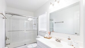 Ein modernes Badezimmer mit Duschkabine aus Glas, einer weißen Toilette, einem Waschtisch mit Spiegel und einem Waschbecken.