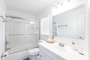 Un baño moderno con cabina de ducha de vidrio, inodoro blanco, tocador con espejo y lavamanos.