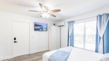 A bedroom with a bed, a ceiling fan, a TV on the wall, and a window with curtains.