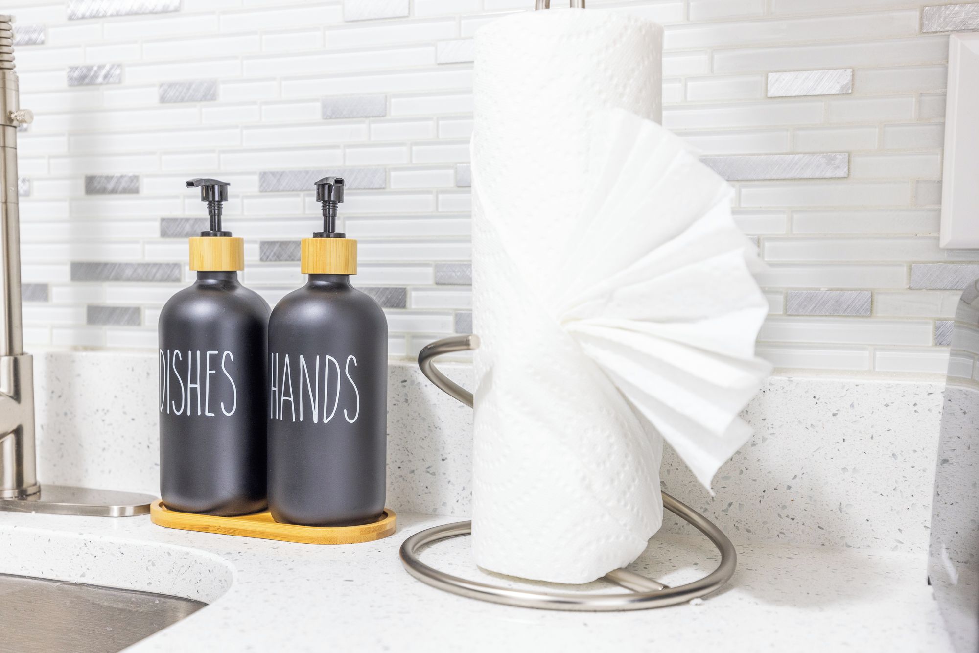 Ein Badezimmer mit einem weißen Handtuchspender, zwei schwarzen Seifenspendern und einer weißen Wand.