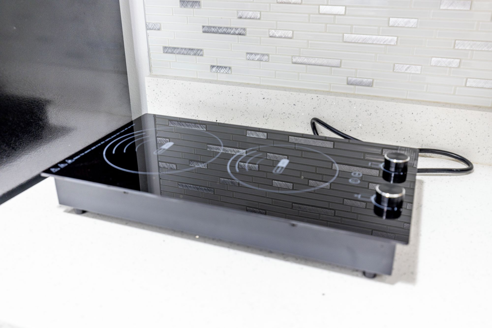 A kitchen with a modern induction cooktop and a white tiled backsplash.