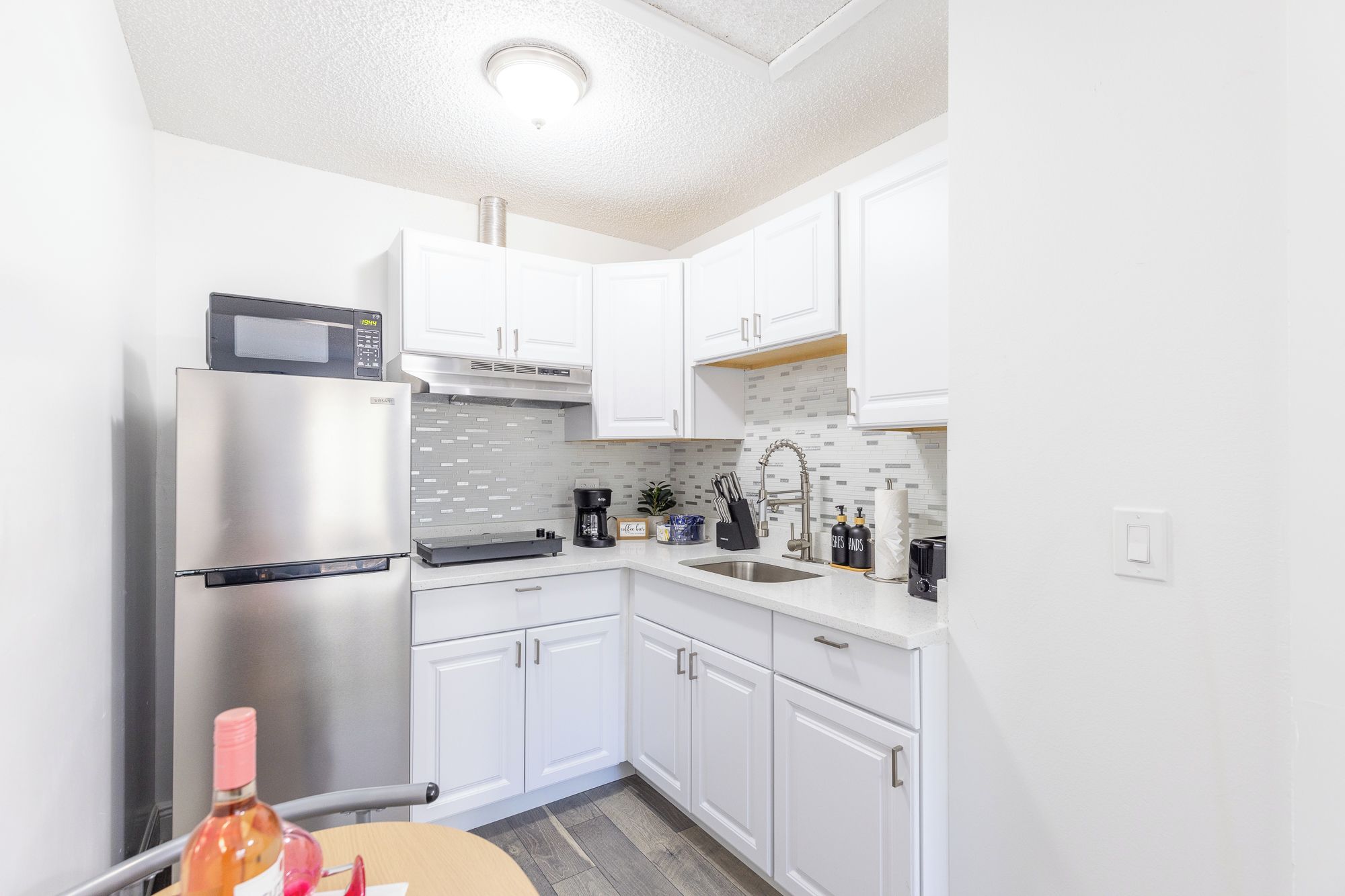 A compact kitchen with white cabinets, a stainless steel refrigerator, a microwave, and a coffee maker.