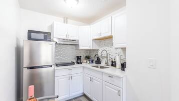 A compact kitchen with white cabinets, a stainless steel refrigerator, a microwave, and a coffee maker.