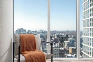 Habitación en un rascacielos con vistas a la ciudad, una silla con una manta y un ventanal grande.