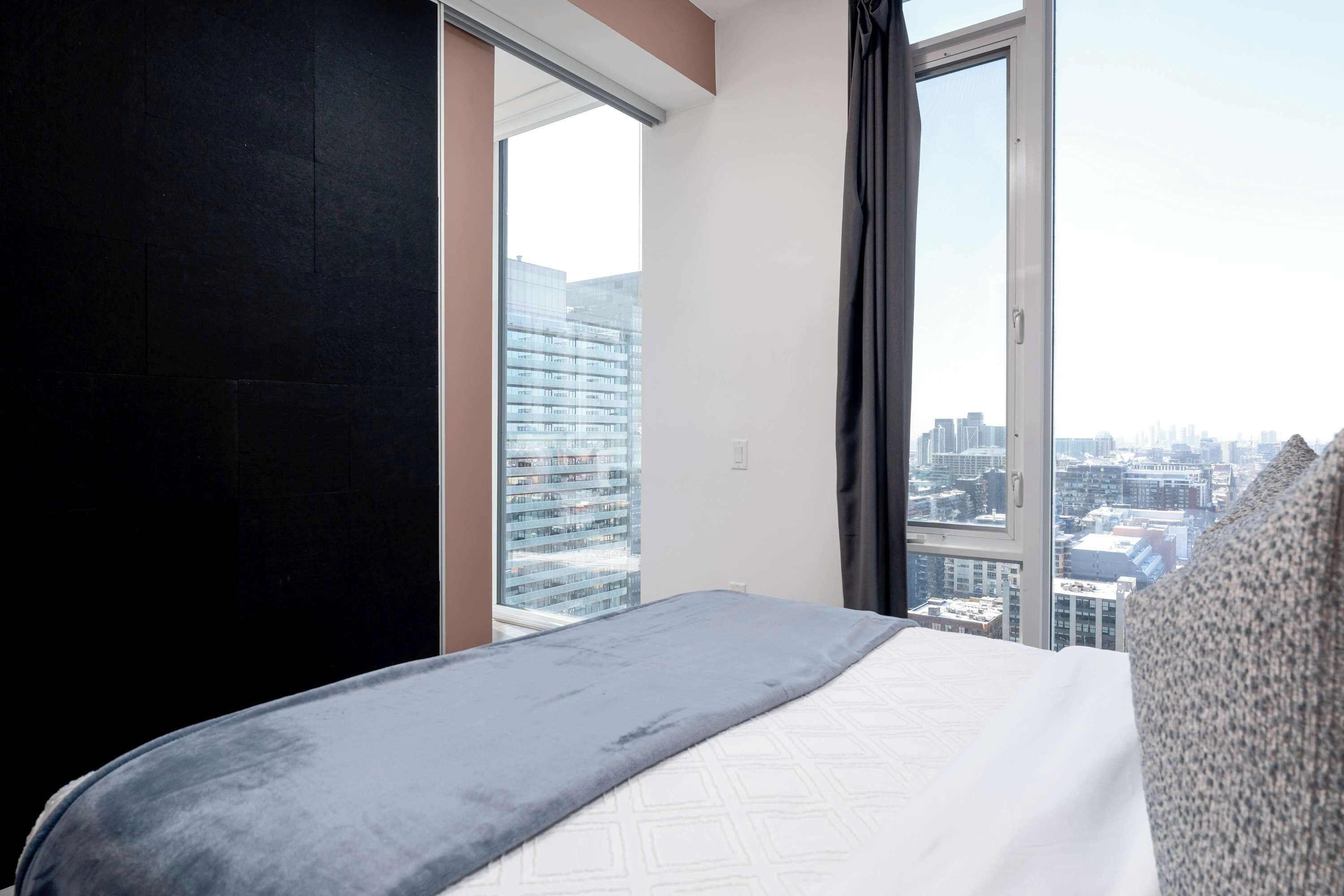 Habitación de hotel con un ventanal grande, una cama y vistas a la ciudad.