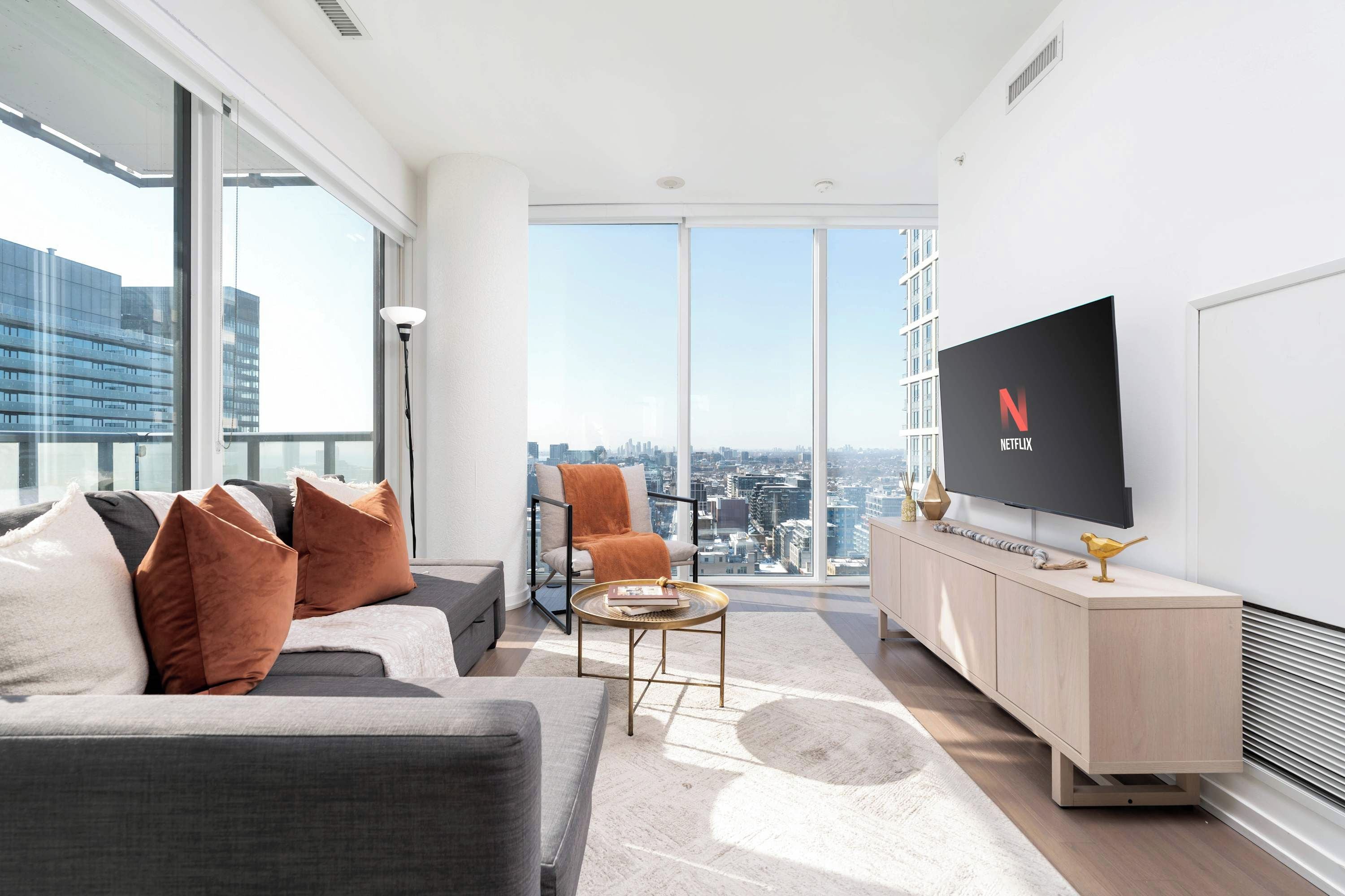 Una sala de estar moderna con un sofá, sillones, una mesa de centro y un televisor en la pared.