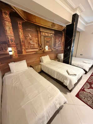 A hotel room with three beds, a large mural on the wall, and a red patterned rug. - Bella Casa Pyramids Inn (El haram)