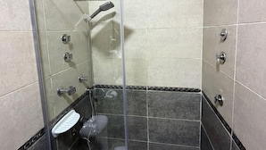 A glass-enclosed shower stall with a handheld showerhead, a glass shelf, and a white step. - Bella Casa Pyramids Inn (El haram)