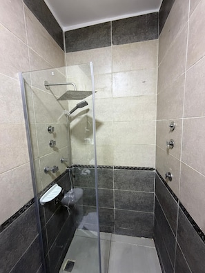 A glass-enclosed shower stall with a handheld showerhead, a glass shelf, and a white step. - Bella Casa Pyramids Inn (El haram)
