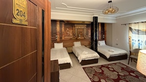 A hotel room with three beds, a large mural, a chandelier, and a wooden door with a number sign. - Bella Casa Pyramids Inn (El haram)