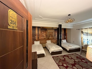 A hotel room with three beds, a large mural, a chandelier, and a wooden door with a number sign. - Bella Casa Pyramids Inn (El haram)