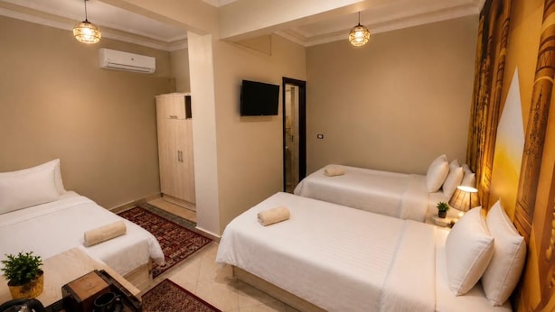 A hotel room with two beds, a TV, an air conditioning unit, and a small table with a plant. - Bella Casa Pyramids Inn (El haram)