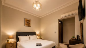 A hotel room with a large bed, bedside lamps, a desk, a chair, and a television. - Bella Casa Pyramids Inn (El haram)