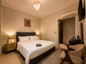A hotel room with a large bed, bedside lamps, a desk, a chair, and a television. - Bella Casa Pyramids Inn (El haram)