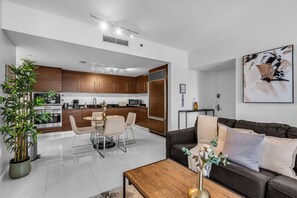 A modern living room with a dark brown sofa, a coffee table, and a dining area with a round table and chairs. - Luxury 1BR + Den | Bay & Pool Views | Brickell (Miami)
