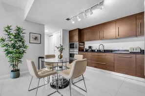 A modern kitchen with wooden cabinets, stainless steel appliances, and a round dining table with chairs. - Luxury 1BR + Den | Bay & Pool Views | Brickell (Miami)