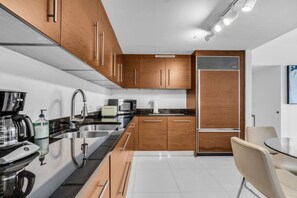 A modern kitchen with wooden cabinets, stainless steel appliances, and a dining area with a table and chairs. - Luxury 1BR + Den | Bay & Pool Views | Brickell (Miami)