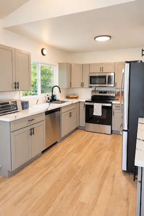 A modern kitchen with light-colored cabinets, stainless steel appliances, and a wooden floor. - Palm Paradise — AC + Gym + Game Room Sleeps 15 (Keaau)