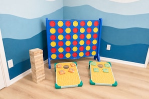 A room with a blue wall, a blue playpen, a wooden block tower, and two small green and yellow play mats. - Palm Paradise — AC + Gym + Game Room Sleeps 15 (Keaau)