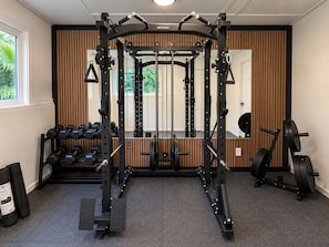 A gym with a squat rack, dumbbells, and weight plates. - Palm Paradise — AC + Gym + Game Room Sleeps 15 (Keaau)
