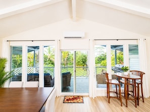A spacious room with a large sliding glass door leading to a balcony, a dining table with chairs, and a small grill on the balcony. - Palm Paradise — AC + Gym + Game Room Sleeps 15 (Keaau)