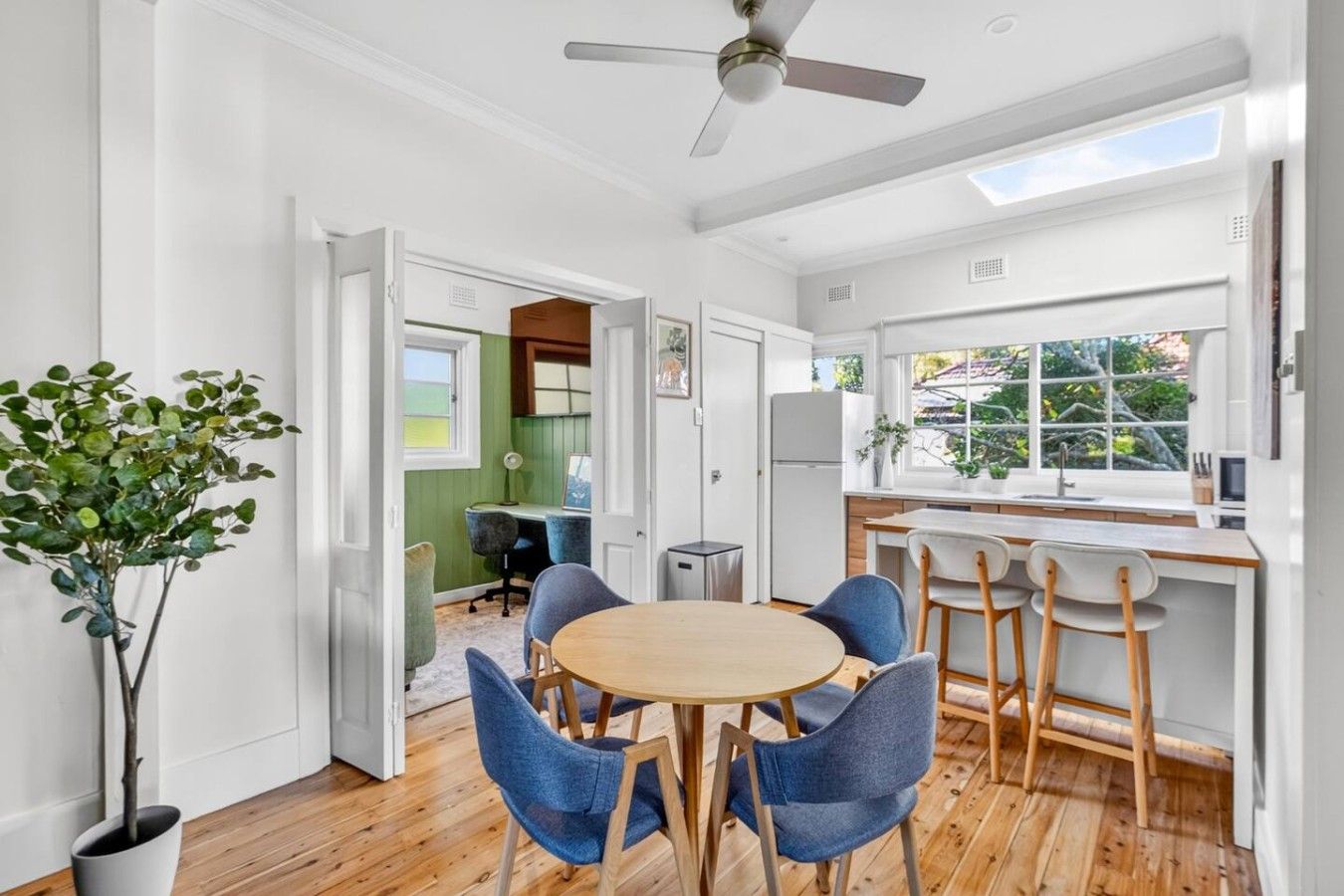 A modern kitchen with a dining area, wooden flooring, and a ceiling fan.