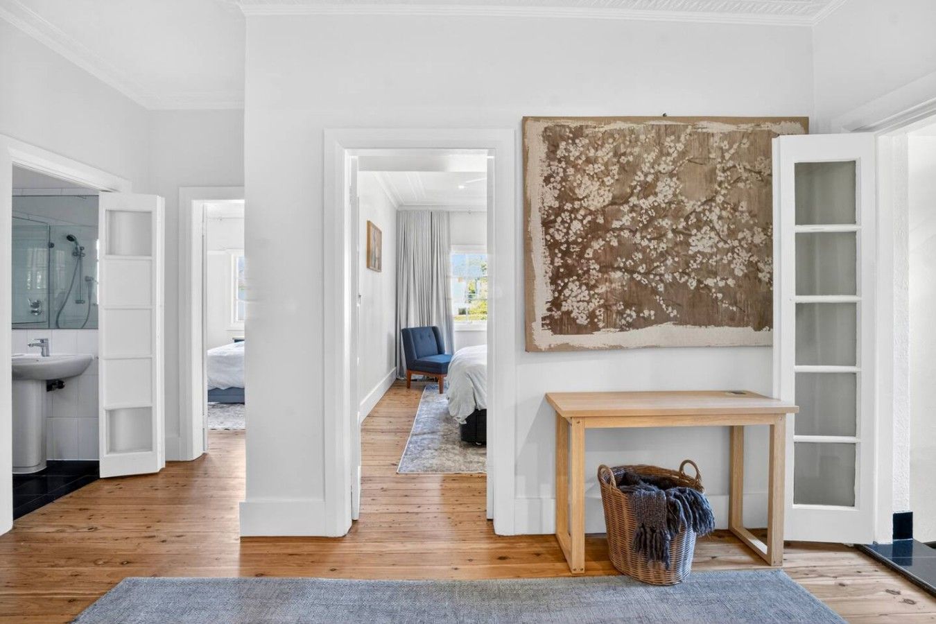 Ein modernes Interieur mit einem Flur, der zu einem Schlafzimmer führt, einem großen abstrakten Gemälde und einem Holztischchen.