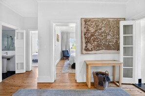A modern interior with a hallway leading to a bedroom, a large abstract painting, and a wooden console table. - Art deco, light
and airy apartment (Cammeray)
