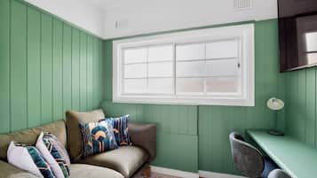 A room with a green wall, a window, a sofa with cushions, a desk, and a chair.