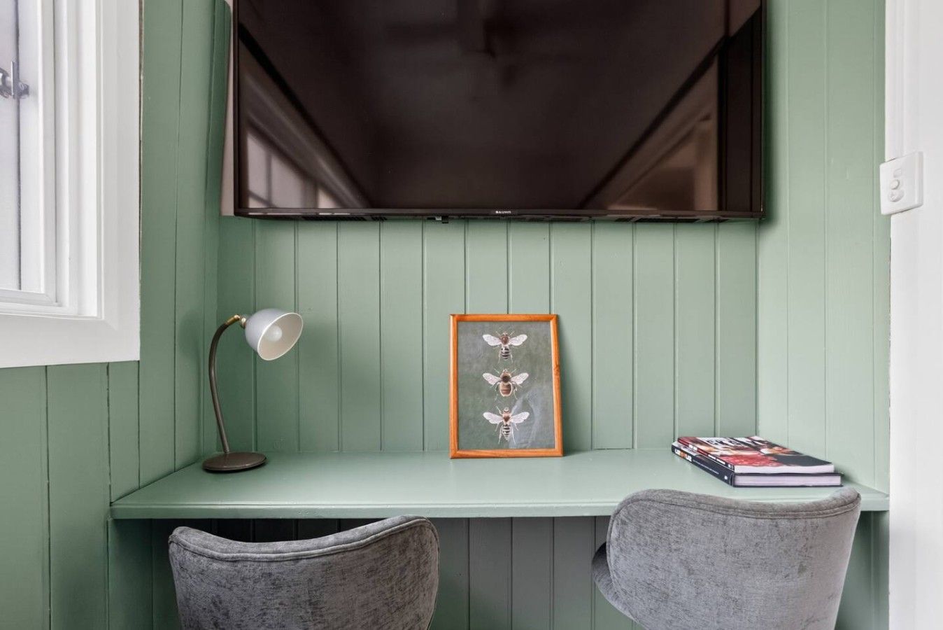 A green-painted desk with a framed picture, a lamp, and a book.