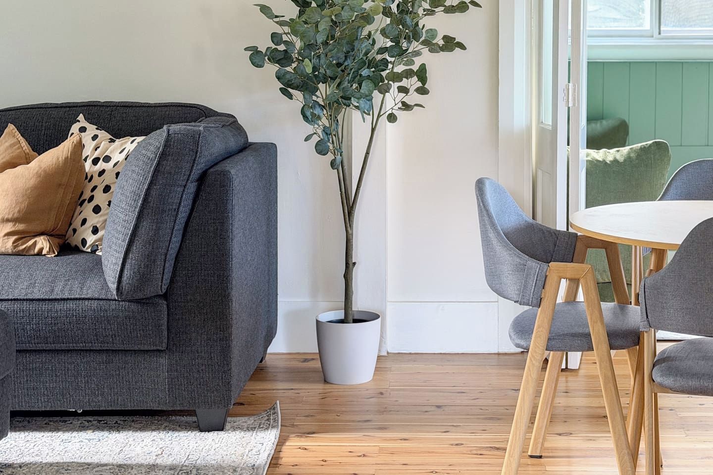 A modern living room with a grey sofa, a potted plant, and a dining area with grey chairs and a round table.