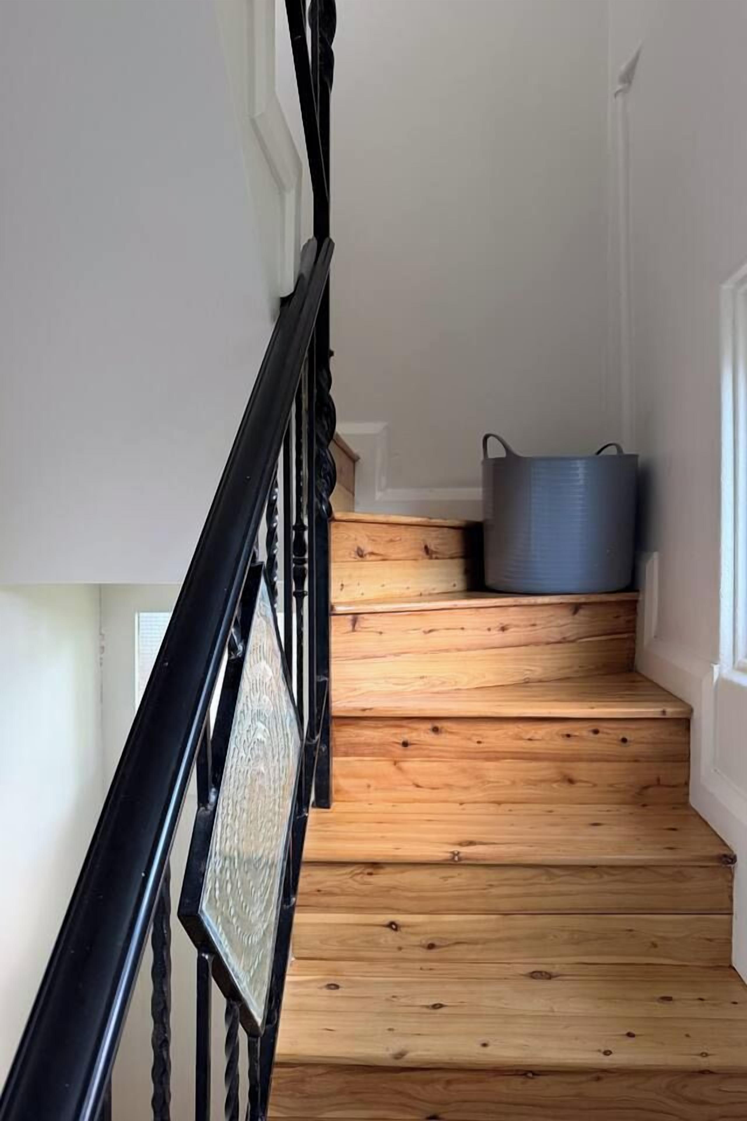 A wooden staircase with a black metal railing and a grey container on the landing.