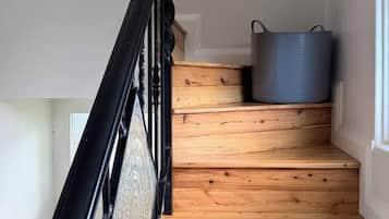 A wooden staircase with a black metal railing and a grey container on the landing.