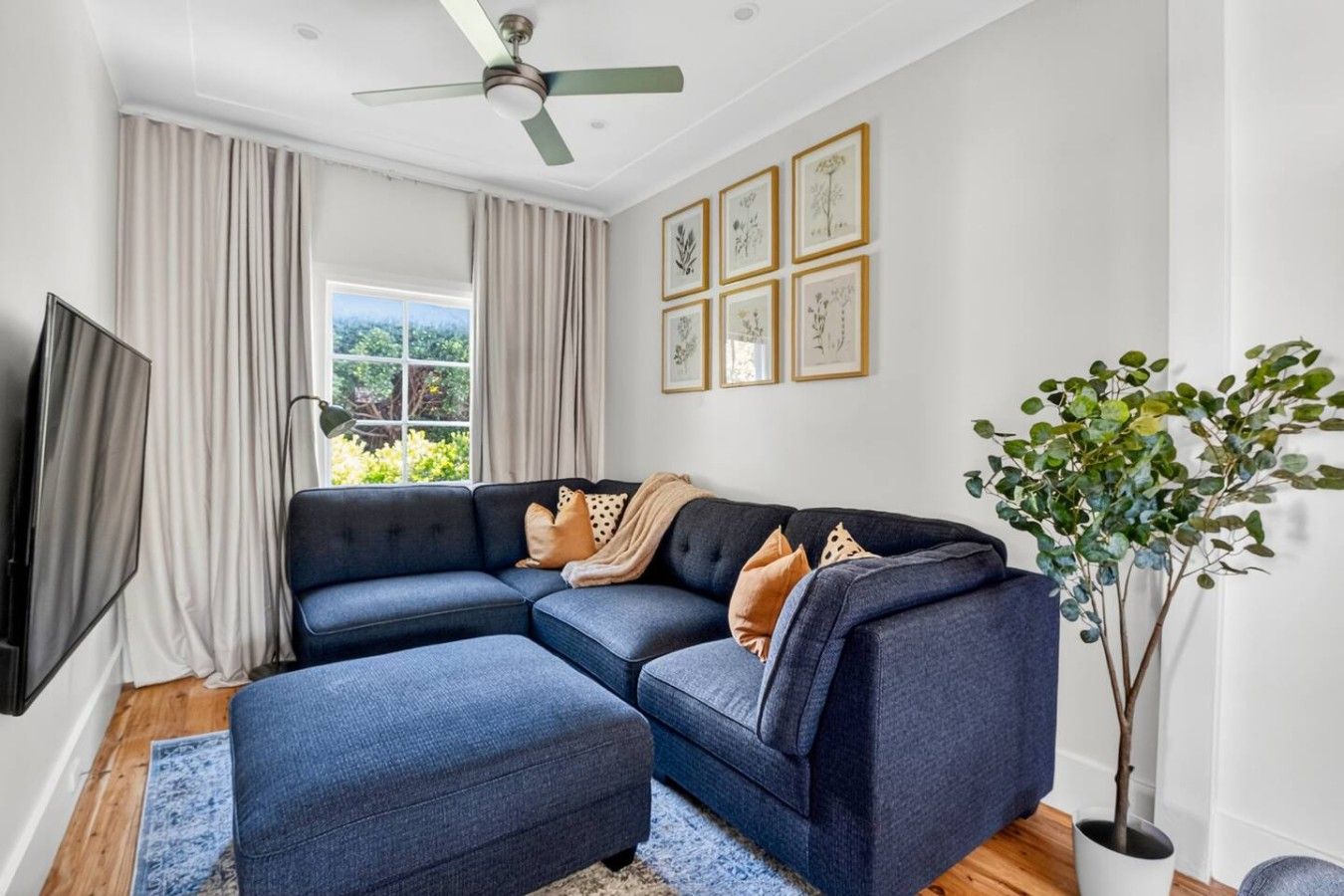 A living room with a sectional sofa, a television, and a ceiling fan.