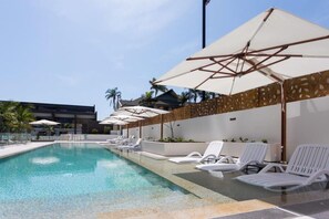 A pool area with lounge chairs and umbrellas, surrounded by a low wall and palm trees. - Coastal Comfort 2Bedroom Luxury Stay w Ocean View (Surfers Paradise)