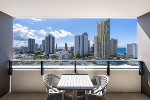 A balcony with a table and two chairs, overlooking a cityscape with high-rise buildings and a clear sky. - Coastal Comfort 2Bedroom Luxury Stay w Ocean View (Surfers Paradise)