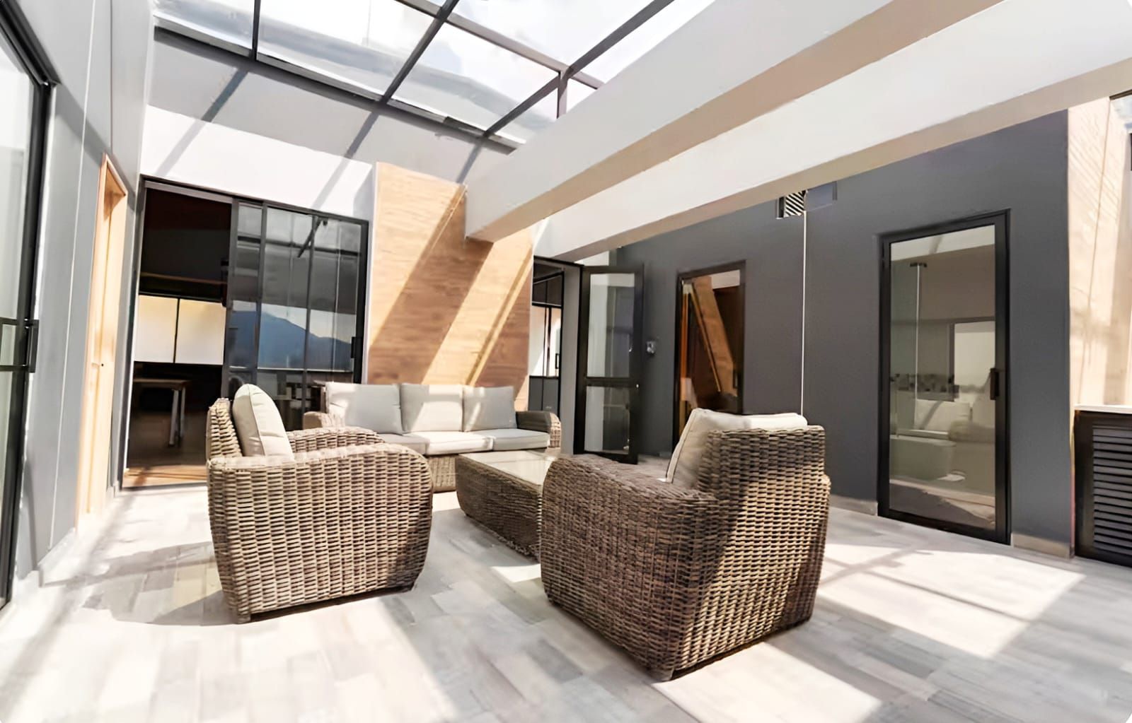 Un espacio exterior moderno con mobiliario de mimbre, una puerta de vidrio que da a un balcón y vistas al interior.