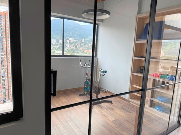 Ein Zimmer mit großem Fenster, Holzboden, Deckenventilator und Blick auf eine Stadtlandschaft mit Bergen.