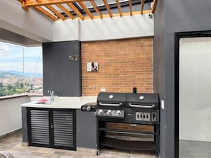 Eine Dachterrasse mit einem Grill, einem Spülbecken und Blick auf die Stadt.