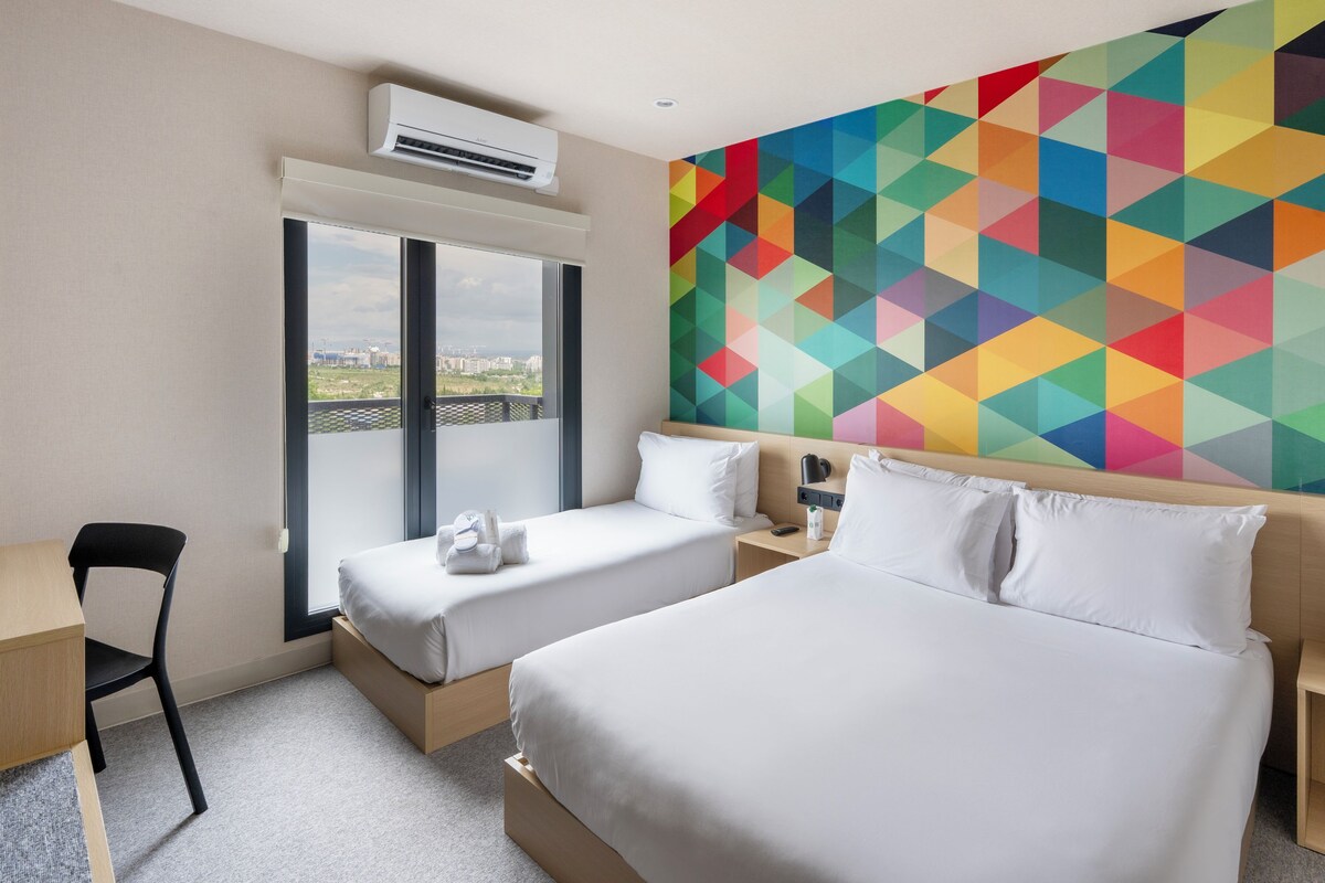 Ein Hotelzimmer mit einem Bett, zwei Nachttischen, einem Sessel, einer Klimaanlage und einem großen Fenster mit Blick.