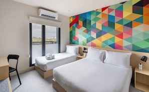 Habitación de hotel con una cama, dos mesitas de noche, una silla, aire acondicionado y un ventanal con vistas.