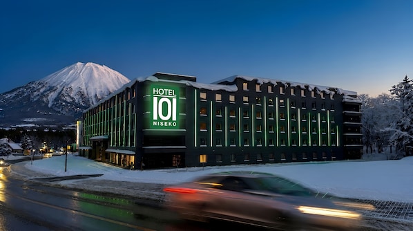 Un edificio de hotel con un cartel llamativo, rodeado de árboles cubiertos de nieve y una montaña al fondo.