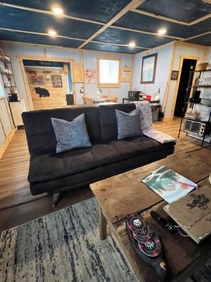 A cozy living room with a dark sofa, patterned cushions, a wooden coffee table, and a television in the background. - Cozy & Quiet Getaway in the Smokies, hot tub, fire pit and more (Newport)