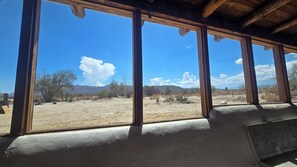 Una habitación con grandes ventanales que ofrecen vista a un paisaje desértico con poca vegetación y montañas distantes.